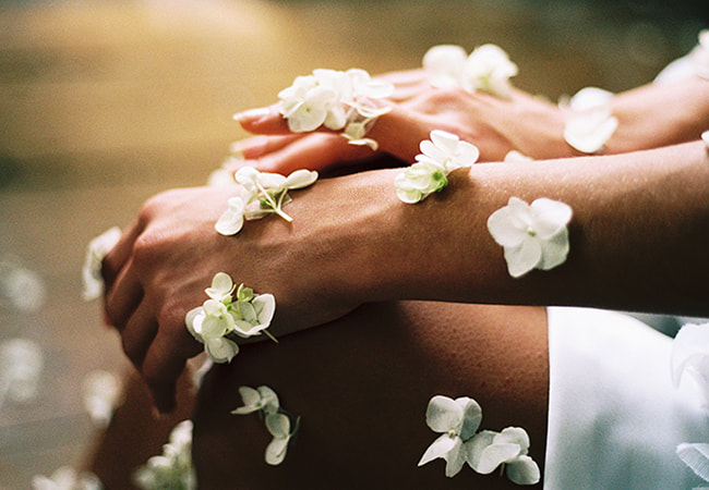 close up image of hands with white flowers placed all around them.