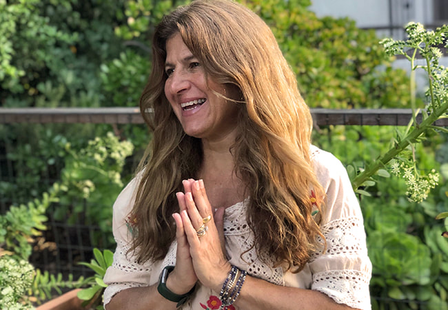 Image of Dr. Jill smiling in a garden with her hands in prayer position