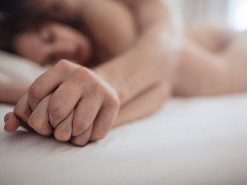 Closeup image of  couple's hands intertwined in bed